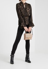 Blusa a maniche lunghe con stampa leopardata, con collo legato e polsini a volant, abbinata a jeans skinny neri e stivali neri alla caviglia. Borsa mini beige.
