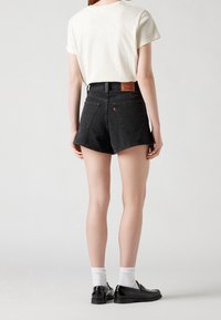 Svarta denimshorts med hög midja, fransad nederkant och bakfickor. Kombinerat med en ljus t-shirt och svarta skor.
