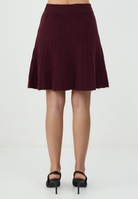 Bordeauxfarbene plissierte Rock aus weichem Stoff, mit einem taillierten Bund und ausgestelltem Saum, versehen mit einer strukturierten Oberfläche.