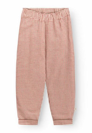 Jambes portant un pantalon ample à carreaux rouges et blancs et un haut assorti, debout pieds nus sur un fond uni gris clair.