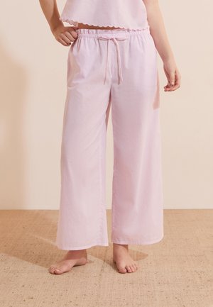 Persona con pantaloni del pigiama larghi a righe rosa e bianche con coulisse in vita, in piedi scalza su un pavimento strutturato.