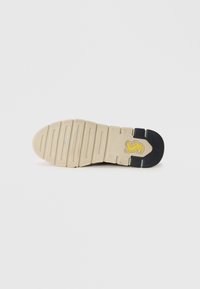 Semelle de chaussure avec une base couleur crème et un talon noir. Présente une texture striée et un logo jaune sur l'arche pour l'adhérence et le branding.