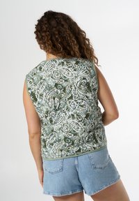 Top verde senza maniche con un motivo floreale e paisley bianco, dalla consistenza liscia e scollatura rotonda, abbinato a pantaloni shorts in denim.