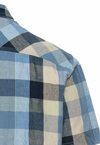 Gros plan de l’épaule et du haut du dos d’une chemise à carreaux bleu, beige et gris avec des coutures visibles et la texture du tissu.