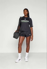 Juodas Adidas sportinis kostiumas, sudarytas iš trumpomis rankovėmis marškinėlių su žaliu logotipu, atitinkančių šortų ir baltų kojinių su juodais akcentais.