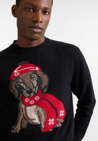 Čierny pletený sveter s motívom psa v červenej čiapke a šále, zdobený bielymi snehovými vločkami, s úzkym dizajnom pri krku.