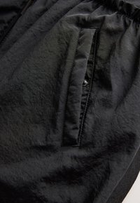 Shorts de sport noirs en tissu léger, dotés d'une taille élastique, de poches latérales et d'une surface lisse légèrement texturée.