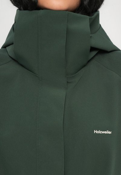 Veste vert foncé à col montant avec une texture lisse, arborant un logo blanc "Holzweiler" à l'avant et des détails de couture minimalistes.
