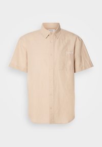 Camicia beige a maniche corte con bottoni, realizzata in cotone, dotata di tasca anteriore e di una piccola toppa con logo sul lato sinistro.