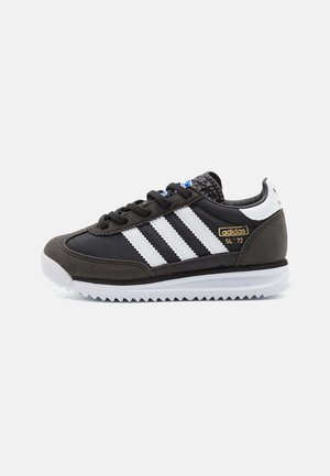 Zwart-witte Adidas SL '72 sneaker met drie witte strepen, zwarte veters en een witte zool met een getande rand.