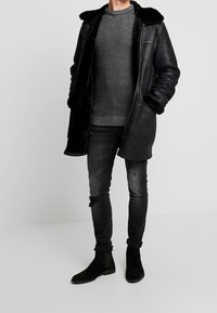 Musta nahkatakki tekoturkiskauluksella, harmaa neulepaita, kulutetut mustat farkut ja mustat mokkanahkaiset nilkkurit. Mukava, teksturoitu muotoilu.