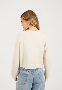 Crème-kleurige, cropped gebreide trui met een zachte textuur, raglanmouwen en ribbelrand, gecombineerd met lichtblauwe spijkerbroek.