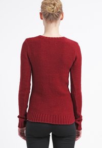 Röd stickad tröja med rundad halsringning, ribbade ärmar och nederkant. Strukturerad textil med en figurnära design, sedd bakifrån.