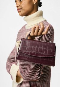 Burgunder faux-krokodil læder håndtaske med en topflap, en kort hank og subtile stikninger. Båret med en stribet sweater.