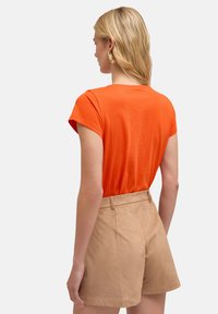 Orange kortærmet top lavet af blødt stof, båret med beige højtaljede shorts, der har en glat tekstur og lige snit.