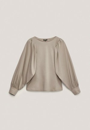 Blouse beige à manches longues avec manches bouffantes ballon et poignets ajustés, encolure ronde, présentée sur un fond clair uni.