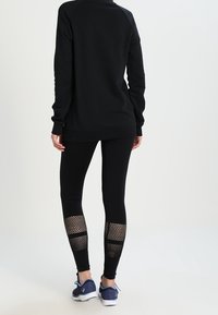 Felpa nera con maniche raglan abbinata a leggings neri con pannelli in rete sui polpacci e una texture liscia. Scarpe da ginnastica completano l'outfit.