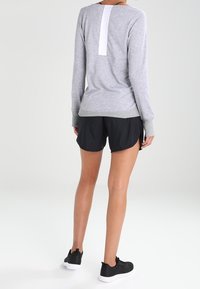 Grå långärmad tröja med ett vitt bakstycke, kombinerad med svarta shorts och svarta sportskor. Mjuk tyg, avslappnad passform och minimalistisk design.