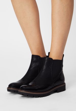 Black Chelsea boots featuring elastic side panels, a glossy leather toe, textured fabric accents, and a rugged rubber sole.