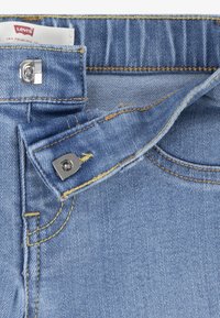 A világoskék farmernadrág strapabíró fém gombos záródással és sárga öltésekkel rendelkezik. Az anyag klasszikus twill mintázatot mutat, elhalványult árnyalatokkal.