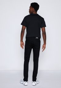 Fekete póló rövid ujjakkal, fekete slim-fit farmerrel és fehér sportcipővel párosítva. Tiszta vonalak, minimalista design, és nincs látható minta.