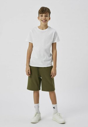 T-shirt en coton blanc associé à un short vert, texturé avec un tissu doux. Des baskets blanches et des chaussettes mi-mollet avec détail de logo complètent le look.