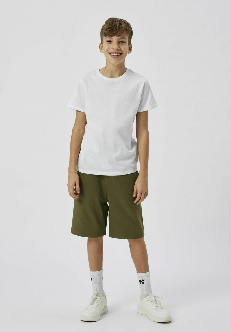 Hvid bomulds t-shirt parret med grønne shorts, struktureret med blødt stof. Hvide sneakers og ankellange sokker med logodetail fuldender looket.