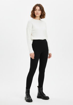White ribbed long-sleeve sweater paired with black ribbed leggings and black lace-up combat boots, standing on a white background.