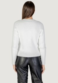 Maglione bianco e soffice a maglia con maniche lunghe, scollatura rotonda e orlo a coste, abbinato a pantaloni in pelle nera. Texture morbida e design pulito.