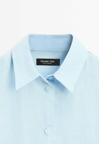 Světle modrá lněná košile s límečkem, s knoflíkovým zapínáním a černou etiketou s nápisem "Massimo Dutti." Texturovaná tkanina.
