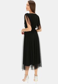 Czarna sukienka z przejrzystymi, krótkimi rękawami i wcięciem w talii, z falbaną z tiulu, w połączeniu z srebrnymi sandałami na wysokim obcasie.