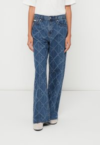 Jeans de ganga azul de corte flare com padrão de diamante, cinco bolsos e fecho de botão. O tecido tem um acabamento ligeiramente texturizado.