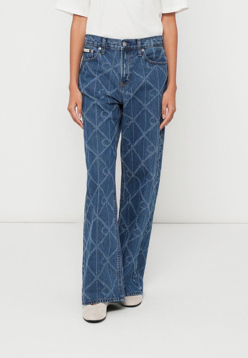 Jeans de ganga azul de corte flare com padrão de diamante, cinco bolsos e fecho de botão. O tecido tem um acabamento ligeiramente texturizado.