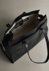 Černá kožená taška přes rameno se strukturovaným designem, světle zbarveným interiérem, dvěma uchy a kapsou na zip.