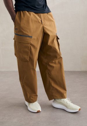 Brown cargo pants with zippered pockets, made of lightweight fabric. Paired with light-colored athletic shoes.