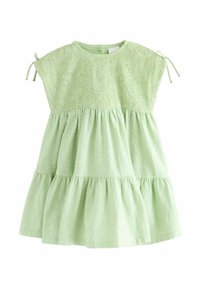Lichtgroene jurk met een textuur kant top, korte mouwen en geplooide lagen bij de taille. Heeft strikaccenten bij de schouders.