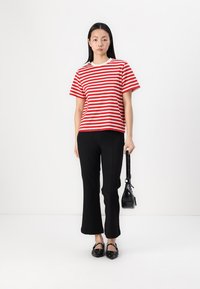 Red and white striped t-shirt with short sleeves, paired with black flared pants. Model holds a small black bag and wears black flats.