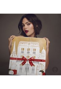 Calendrier de l'Avent L'Oréal avec un design doré et blanc incluant des monuments parisiens, orné d'un ruban rouge portant l'inscription "TU LE VAUX BIEN".