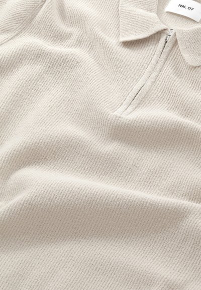 Lys beige polo-style sweater med en tekstureret ribbet overflade, der har en halv lynlås og en lille krave.