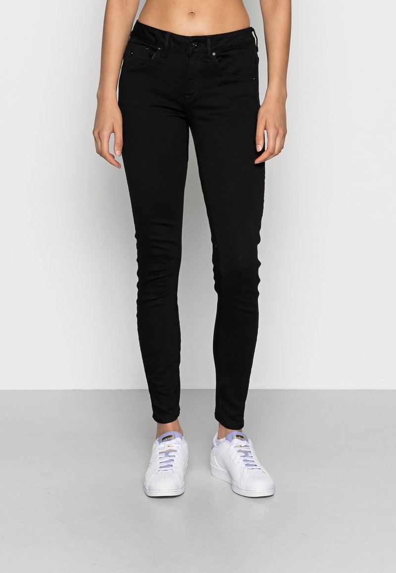 Jean skinny noir en denim, avec un design classique à cinq poches, une coupe ajustée, et associés à des baskets blanches.