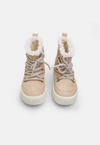 Bottines beiges claires avec doublure en fausse fourrure, tige en daim texturé et semelle en caoutchouc blanche épaisse. Présente des lacets gris et une fermeture éclair sur le côté.