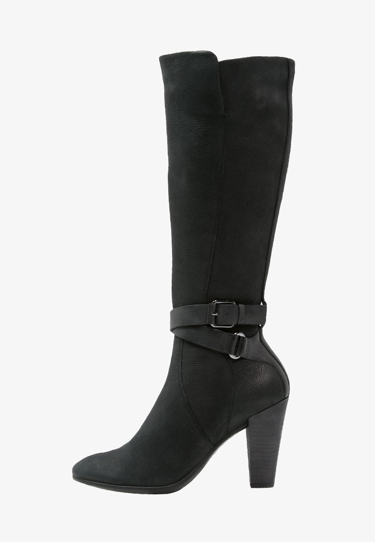 Botte en cuir noire mi-mollet avec un bout pointu, un talon haut empilé et une sangle décorative à boucle autour de la cheville.