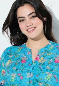 Blusa floreale blu con vivaci fiori rosa e gialli, dotata di scollatura a V, pieghe sottili e una texture di tessuto morbido.