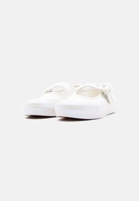 Ζευγάρι λευκά παπούτσια Mary Jane από καμβά με παχιά ελαστική σόλα και ρυθμιζόμενα λουράκια, εμφανιζόμενα πάνω σε απλό φωτεινό φόντο.