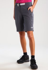 Grå, lätta utomhusshorts med ett bälte, sidofickor och en logotyp på underbenet, tillsammans med svarta atletiska skor och mörka strumpor.