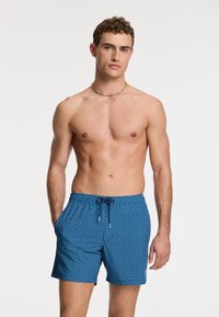 Kék fürdőshorts, gyémántmintával, rugalmas derékpánttal és zsinórral. Könnyű anyag, térd felett érkező hossz.