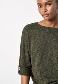 Dark green sweater with a textured knit pattern, loose fit, and rolled sleeves. Features a wide neckline and soft, lightweight material.