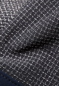 Granatowy materiał z białym wzorem geometrycznym, charakteryzujący się teksturowanym splotem i małymi wypukłymi kropeczkami, tworzącymi skomplikowany detal powierzchni.