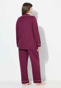 Completo pigiama color marsala realizzato in tessuto morbido, composto da una maglia a maniche lunghe con colletto e piping bianco, e pantaloni a gamba ampia con polsini coordinati.