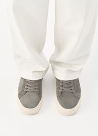 Γκρίζα σουέντ αθλητικά παπούτσια με στρογγυλή μύτη και κρεμ σόλα, που διαθέτουν επίπεδους κορδόνες και ελάχιστη ραφή. Φοράνε με λευκά, φαρδιά παντελόνια.
